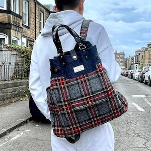 May include: A person wearing a white hoodie carries a gray and red plaid tote bag with black leather straps and a blue denim pocket. The bag has a gold button on the front.