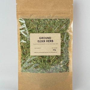 Könnte beinhalten: Ein brauner Papierbeutel mit einem durchsichtigen Plastikfenster, in dem gemahlene Geißfuß-Kräuter zu sehen sind. Das Etikett lautet "GROUND ELDER HERB", "Aegopodium podagraria cut and dried herb 100%", "best before" und "net weight 50g".