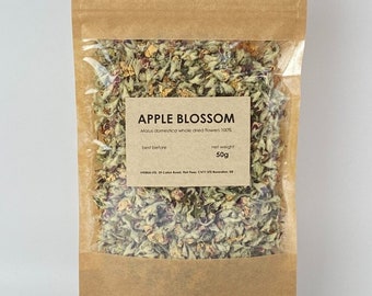 Op de afbeelding: Een bruine papieren zak met een transparant plastic venster dat gedroogde appelbloesems laat zien. Het etiket vermeldt "APPLE BLOSSOM Malus domestica whole dried flowers 100% net weight 50g".