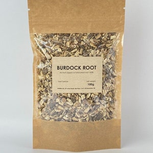 Puede incluir: Una bolsa de papel marrón con una ventana de plástico transparente que contiene raíz de bardana seca. La bolsa tiene una etiqueta que dice "Burdock Root", "Arctium lappa cult and dried root 100%", "best before" y "net weight 100g".