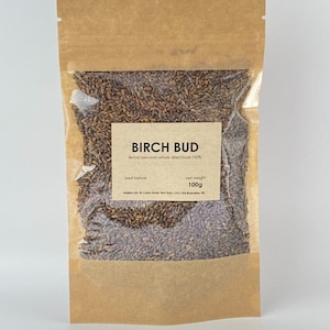Może przedstawiać: Brązowa papierowa torebka z przezroczystym okienkiem, w którym widoczne są brązowe pąki brzozy. Torebka ma etykietę z napisem "Birch Bud Betula pendula whole dried buds 100%" i "waga netto 100g".