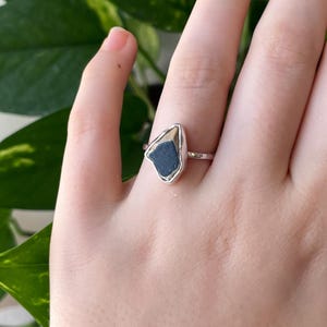 May include: A silver ring with a dark grey stone set in a triangular shape.