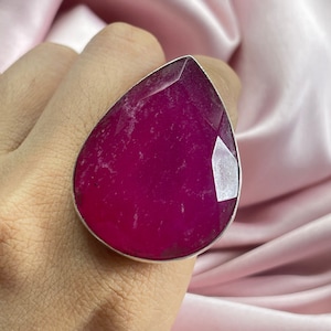 Op de afbeelding: Een ring in de vorm van een traan met een grote, gefacetteerde, roze edelsteen gezet in een zilveren band.