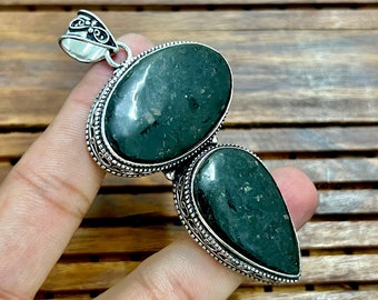 May include: A silver pendant with two green gemstone drops. The pendant has an ornate design with intricate details.