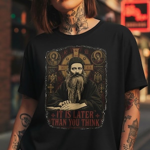 May include: Black t-shirt featuring a religious icon with a long beard and the text "IT IS LATER THAN YOU THINK" in red. The graphic includes a cross and other religious symbols in gold and brown tones.