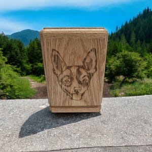 Op de afbeelding: Een houten doos met een lasergegraveerd beeld van een hondenkop. De doos is gemaakt van lichtbruin hout en heeft een natuurlijke houten afwerking.