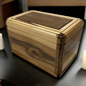 以下が含まれることがあります： クルミの天板と明るい木製の底を持つ木製の箱。箱の上部と側面には装飾的な象嵌が施されています。