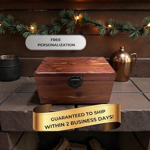 May include: A rectangular wooden box with a hinged lid and a decorative clasp. The box is made of reddish-brown wood and has a dark metal clasp. The text "FREE PERSONALIZATION" is above the box. A gold banner reads "GUARANTEED TO SHIP WITHIN 2 BUSINESS DAYS!"