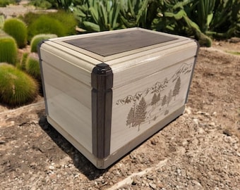 May include: A wooden box with a walnut top and a light wood body. The box has a mountain scene engraved on the front.