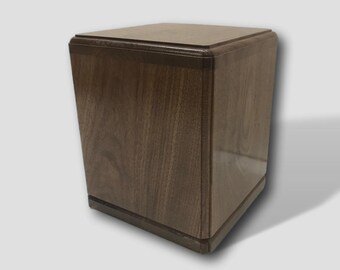 May include: A square wooden box with a dark brown finish. The box has a smooth surface and a slightly raised edge around the top.