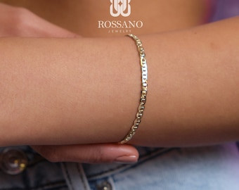 Könnte beinhalten: Ein goldenes Kettenarmband mit einem Ankerketten-Design. Das Armband befindet sich am Arm einer Person.