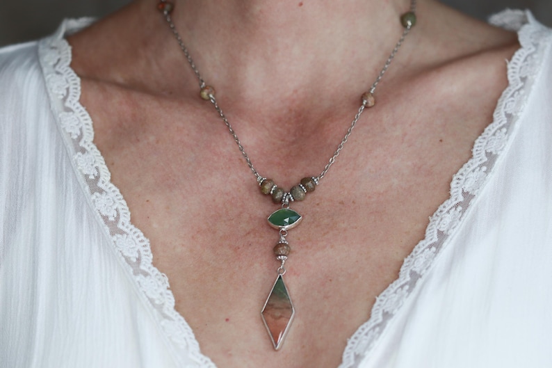May include: A silver chain necklace with brown and green gemstone beads. The necklace has a long pendant with a green gemstone at the top and a large, diamond-shaped, multi-colored gemstone at the bottom.