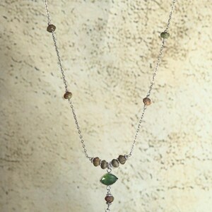 May include: A silver chain necklace with a green and brown stone pendant. The pendant is a teardrop shape with a smaller green stone above it. The chain is adorned with small brown beads.
