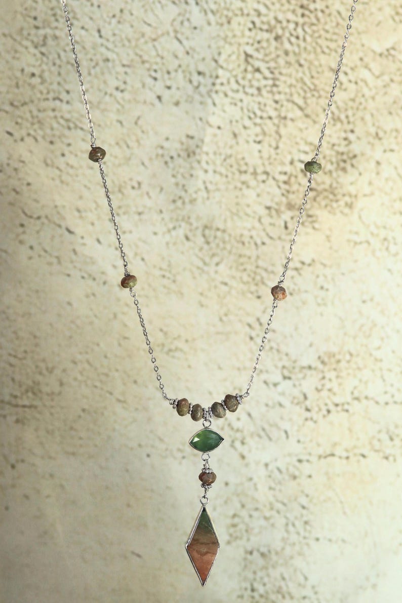 May include: A silver chain necklace with a green and brown stone pendant. The pendant is a teardrop shape with a smaller green stone above it. The chain is adorned with small brown beads.