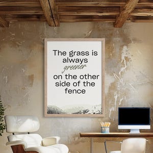 May include: A framed print with a white background and black text that reads "The grass is always greener on the other side of the fence". The print is hanging on a wall with a rustic, brown texture.