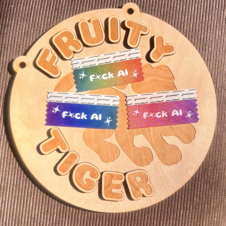May include: A round wooden sign with the words "FRUITY TIGER" in raised, orange-brown letters. The sign features a tiger shape and three colorful tape strips with the text "F*ck AI". The sign has a natural wood grain.