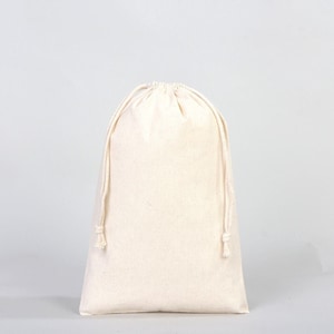 Pode incluir: Uma bolsa creme com cordão feita de tecido. A bolsa é fechada na parte superior com um cordão e tem um fundo arredondado. O fundo é de cor cinza claro sólido.