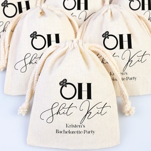 May include: Set of small white fabric bags with black drawstring closures. Each bag has a black and white graphic of a diamond ring with the text "OH Shit Kit" and the name of the event, "Kristen's Bachelorette Party".