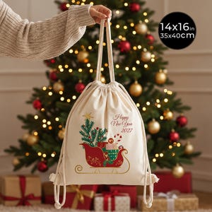 Può includere: Uno zaino a sacca color crema con una grafica di una slitta rossa piena di regali e un albero di pino, con il testo "Happy New Year 2027" stampato in rosso. La borsa misura 35x40cm e include due lunghe tracolle in corda bianca.