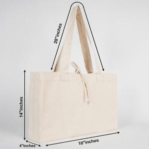 May include: A beige tote bag with long handles. The bag is 18 inches wide, 14 inches tall, and 4 inches deep. The handles are 28 inches long. The bag has a drawstring closure and is made of a sturdy fabric.