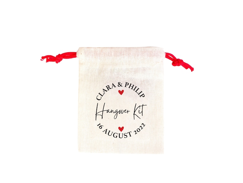 May include: A white cotton drawstring bag with a red drawstring. The bag has a black circle with the text "Clara & Philip" and a red heart. The text "Hangover Kit" is written in cursive below the circle. The date "16 August 2022" is written below the text.