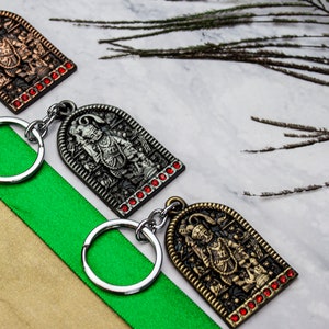 May include: Three keyrings with ornate metal charms featuring a religious figure. The charms are gold, silver, and bronze with red gemstone accents.