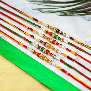 May include: Six colourful bracelets with beads and decorative elements. The bracelets are made of red, yellow, and green thread. The beads are white, red, green, and gold.