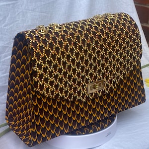 Peut inclure: Un sac à main brun et or avec une bandoulière chaîne et un motif géométrique. Le sac est recouvert de perles dorées.