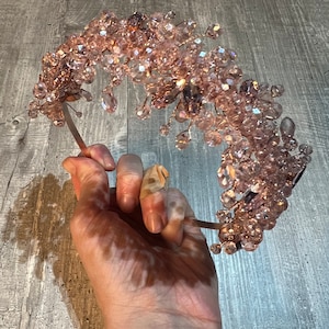 Puede incluir: Una diadema delicada adornada con una cascada de cristales rosas. La diadema está hecha de un metal fino y flexible y es perfecta para añadir un toque de brillo a cualquier atuendo.