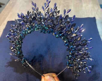 Può includere: Tiara artigianale con montatura in metallo scuro, ornata di cristalli blu e verde acqua. I cristalli sono disposti in un motivo floreale e a forma di foglia, creando un copricapo scintillante ed elegante. Adatta per occasioni speciali.