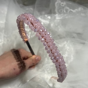 Pode incluir: Uma tiara rosa com contas e uma faixa de metal em ouro rosa. A tiara é adornada com fileiras de pequenas contas rosas facetadas. O design é elegante e adequado para ocasiões especiais ou para uso diário.