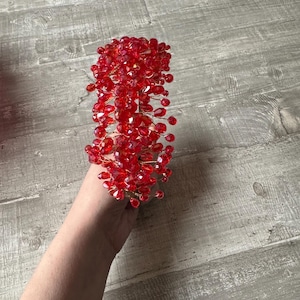 Op de afbeelding: Een rood kralen haarband met een cluster van kleine, druppelvormige kralen. De haarband is gemaakt van draad en is flexibel.