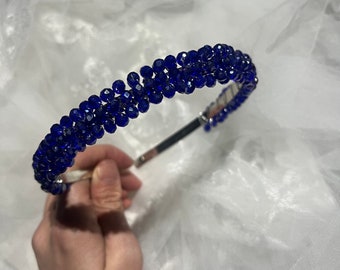 Può includere: Un cerchietto di cristallo blu con una fascia di metallo argentato. Il cerchietto è fatto di piccoli cristalli rotondi che sono infilati in una fila continua.