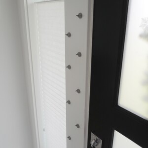 May include: A white door with a black door frame and a silver door handle. There are several small silver hooks on the white door frame.