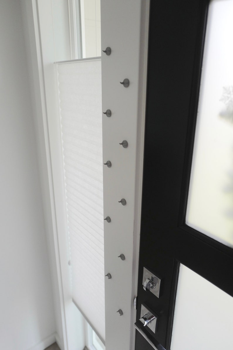May include: A white door with a black door frame and a silver door handle. There are several small silver hooks on the white door frame.