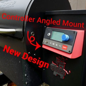 Könnte beinhalten: Ein schwarzer Traeger-Grill mit einer roten Controller-Halterung. Der Controller ist abgewinkelt und verfügt über ein digitales Display und einen Drehknopf. Der Text "New Design" ist auf dem Grill geschrieben.