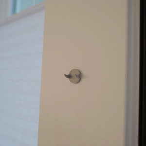 May include: A white wall with a small, round, silver hook attached to it.