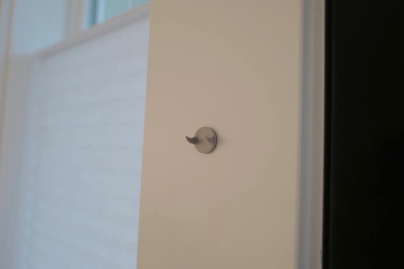 May include: A white wall with a small, round, silver hook attached to it.