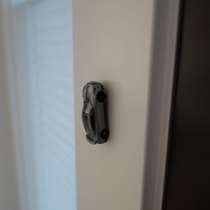 May include: A silver toy car is attached to a white wall with a magnet.