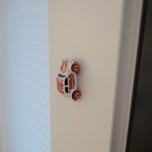 May include: A white toy car with orange and black floral designs on the sides. The car has red wheels with yellow rims.