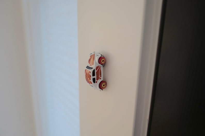 May include: A white toy car with orange and black floral designs on the sides. The car has red wheels with yellow rims.