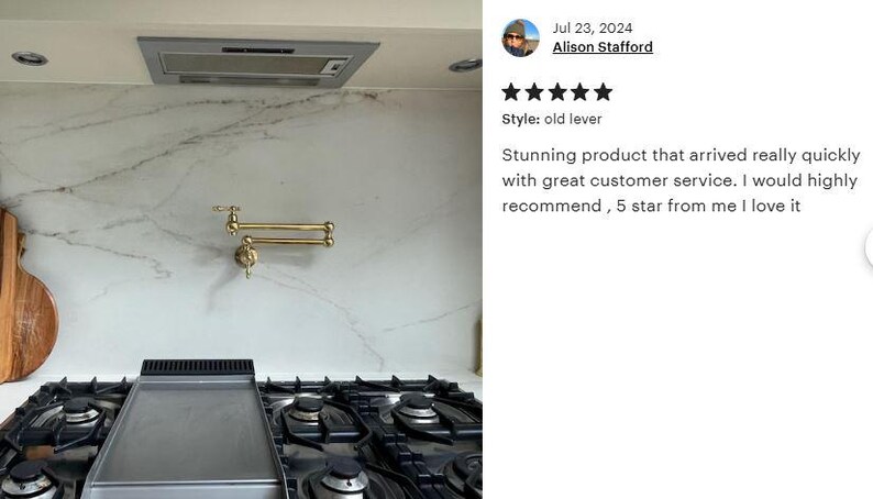 May include: A gold-toned kitchen faucet with a pull-down sprayer mounted on a white marble backsplash. The faucet has a lever handle and a swivel spout. The backsplash is accented with a gray veined pattern.  The faucet is installed above a black gas stovetop with a stainless steel griddle.