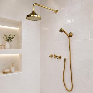 May include: A gold shower system featuring a large round overhead shower head, a handheld shower head with a flexible hose, and three cross-handle valves mounted on a white subway tile wall with two recessed shelves containing toiletries.