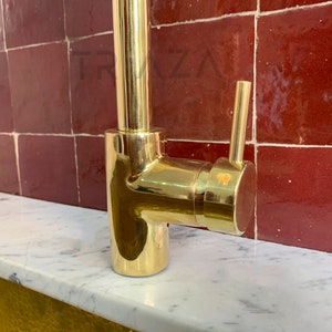 May include: A gold-toned kitchen faucet with a single lever handle and a swivel spout. The faucet is mounted on a white countertop.