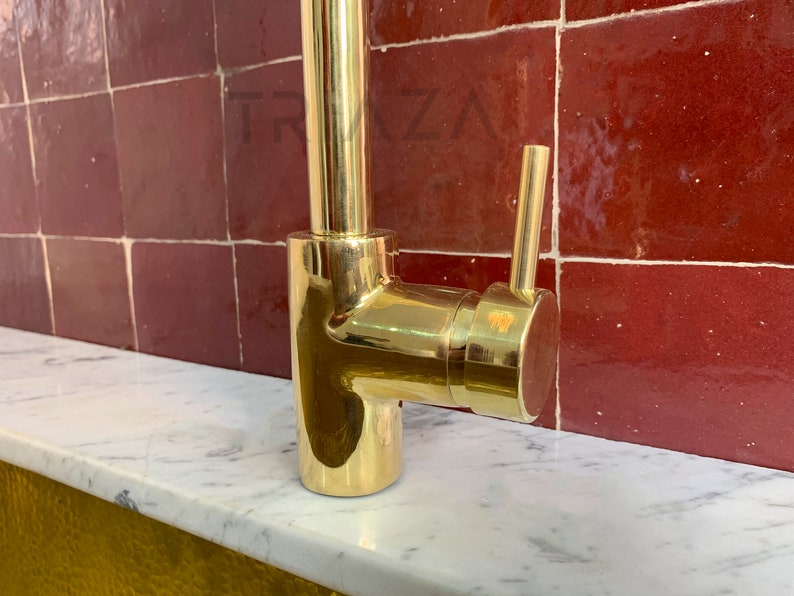 May include: A gold-toned kitchen faucet with a single lever handle and a swivel spout. The faucet is mounted on a white countertop.