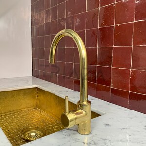 May include: A gold kitchen sink with a matching gold faucet against a backdrop of red tile.