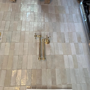 May include: A gold-toned towel rack with two bars and a decorative knob on each end. The rack is mounted on a white tiled wall.