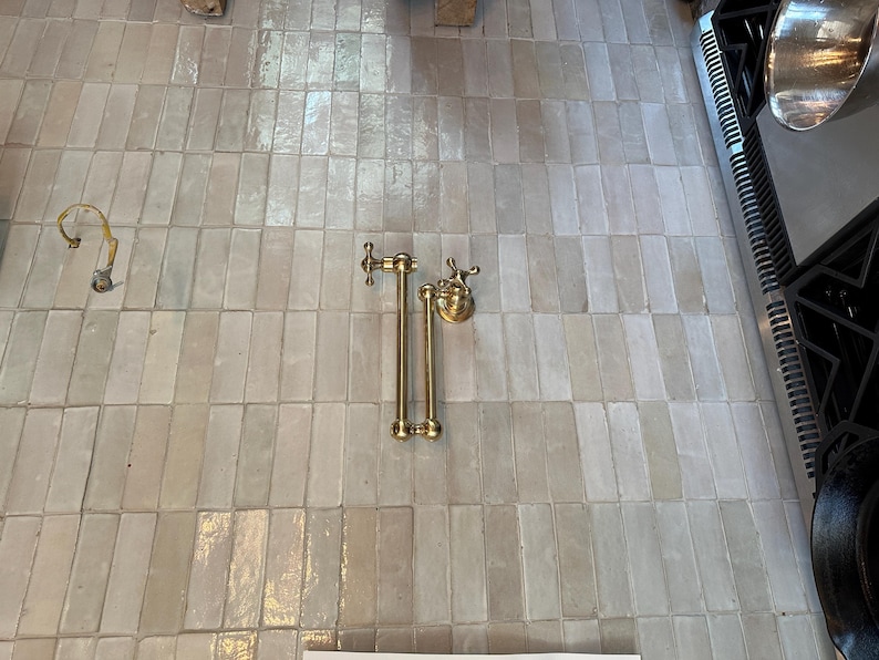 May include: A gold-toned towel rack with two bars and a decorative knob on each end. The rack is mounted on a white tiled wall.