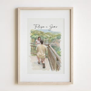 May include: Framed watercolour print showing a proposal scene. A man kneels before a woman on a wooden bridge with a waterfall backdrop. The text "Filipa e João" is written above the couple in the artwork. The frame is light wood.