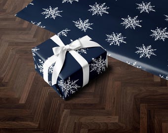 May include: A navy blue gift box with a white ribbon and snowflake pattern. The box is sitting on a dark wood floor.